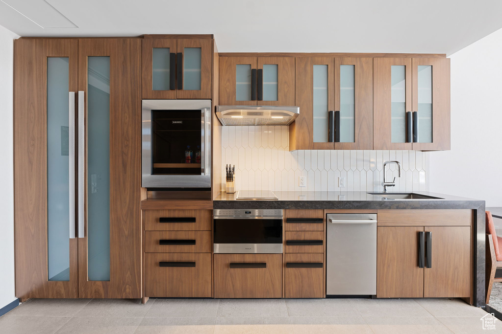 Kitchen featuring oven, wall oven, tasteful backsplash, sink, and wall chimney exhaust hood
