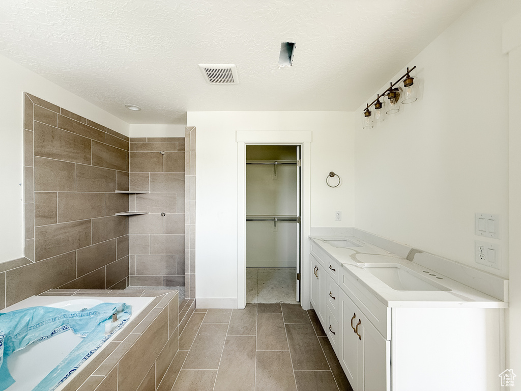 Full bathroom with a bath, tiled shower, a spacious closet, double vanity, and a textured ceiling