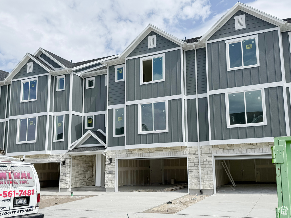 View of front of house with an attached garage, board and batten siding, concrete driveway, and stone siding