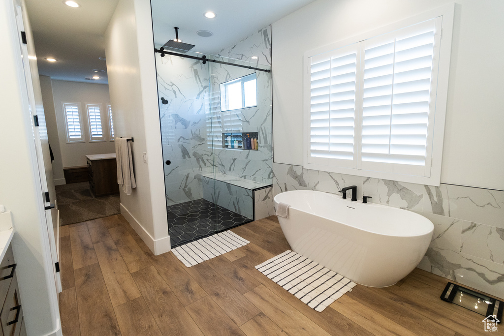 Bathroom with wood-type flooring, separate shower and tub, plenty of natural light, and tile walls