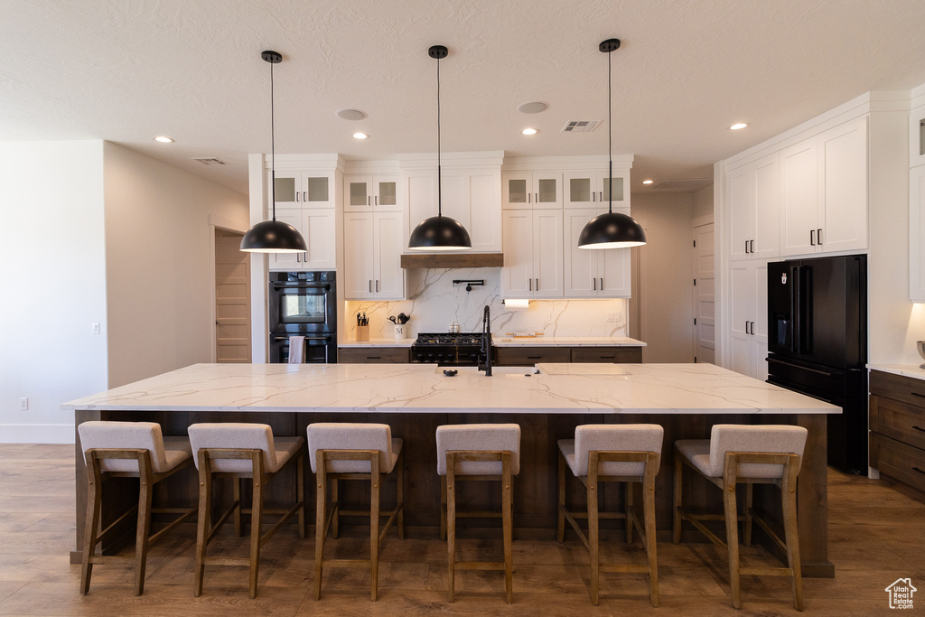Kitchen with white cabinetry, light stone countertops, black appliances, and a spacious island