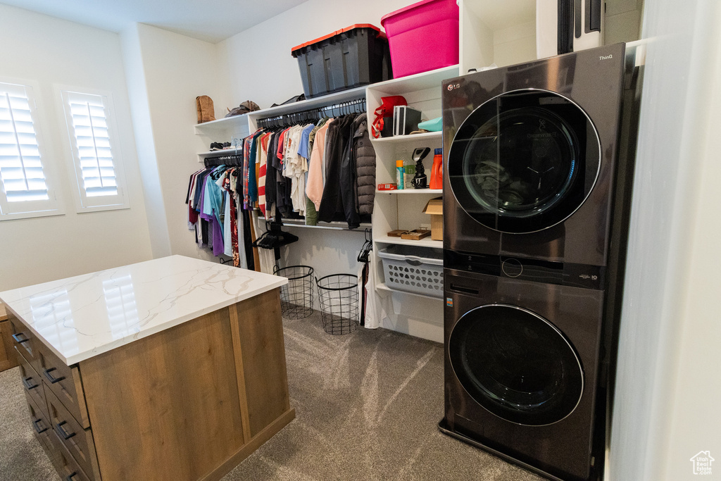 Laundry room featuring stacked washer and clothes dryer and dark carpet
