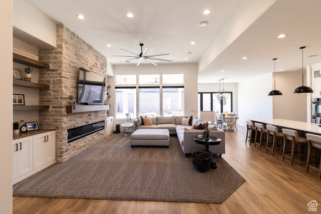 Living room with a large fireplace, ceiling fan, and light wood-type flooring