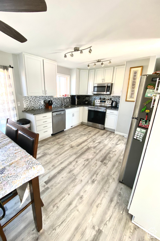Kitchen with tasteful backsplash, stainless steel appliances, light hardwood / wood-style floors, and white cabinets