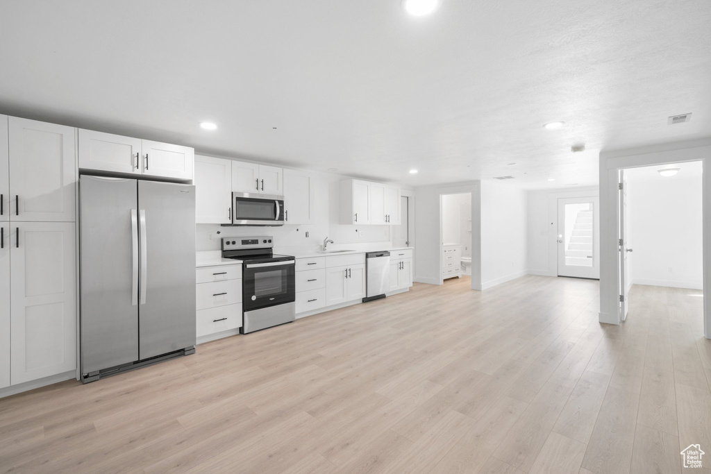 Kitchen with sink, light hardwood / wood-style floors, white cabinets, and appliances with stainless steel finishes