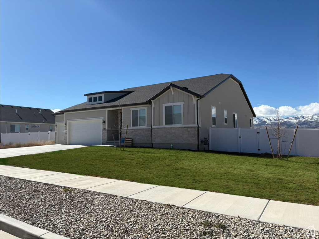 View of front facade with board and batten siding, fence, a garage, driveway, and a front lawn