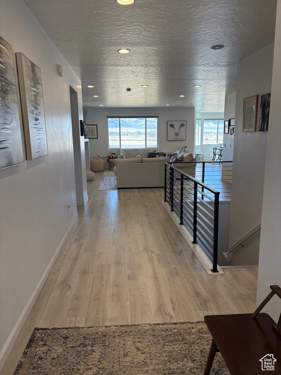 Hall with a textured ceiling, recessed lighting, an upstairs landing, baseboards, and light wood-style floors