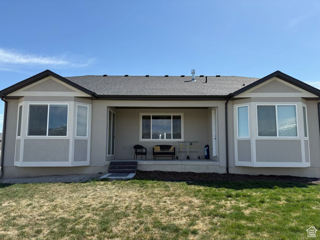 Back of house featuring a yard, stucco siding, and roof with shingles