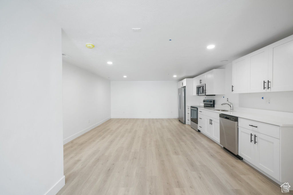 Kitchen with sink, light wood-type flooring, white cabinets, and appliances with stainless steel finishes