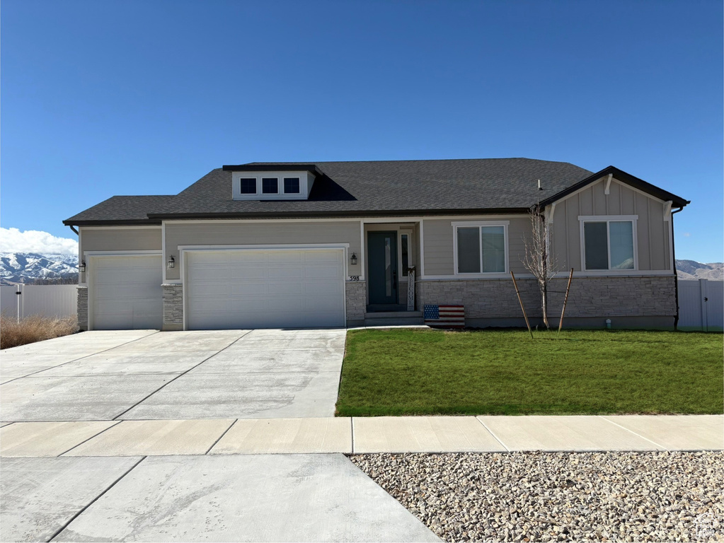 View of front of property with an attached garage, a mountain view, a front lawn, and board and batten siding