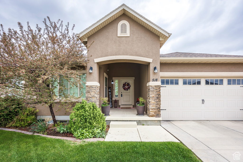 Property entrance featuring stucco siding, stone siding, a garage, and concrete driveway
