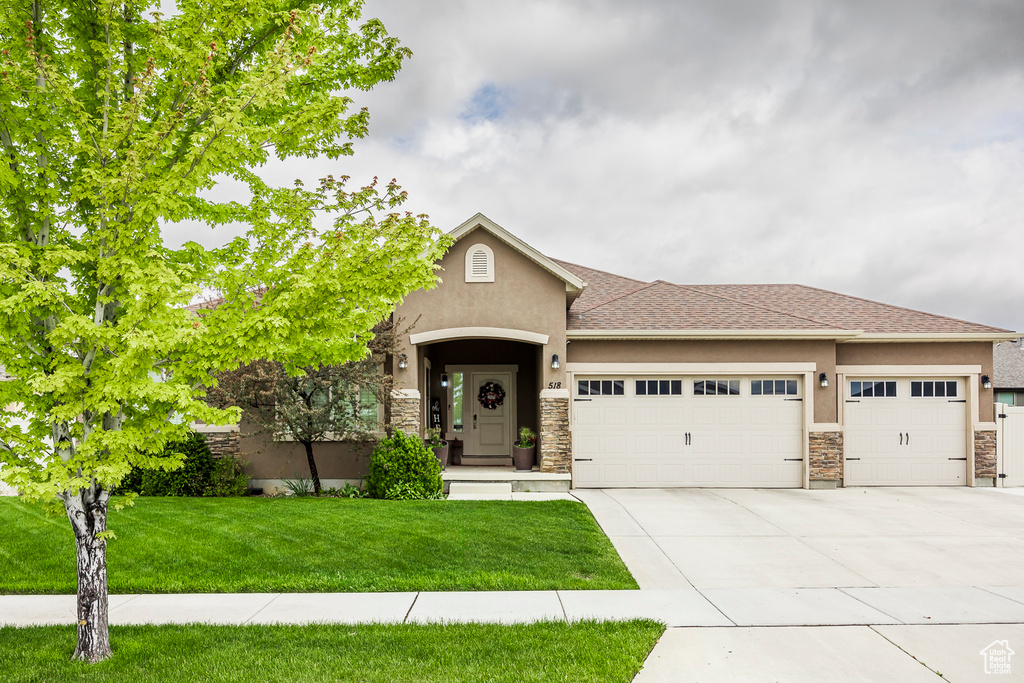 View of front facade with a garage, stucco siding, concrete driveway, stone siding, and a front yard