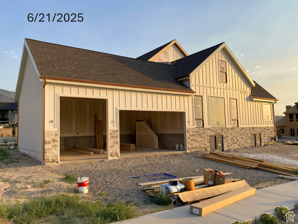 View of side of property with board and batten siding, an attached garage, roof with shingles, and stone siding
