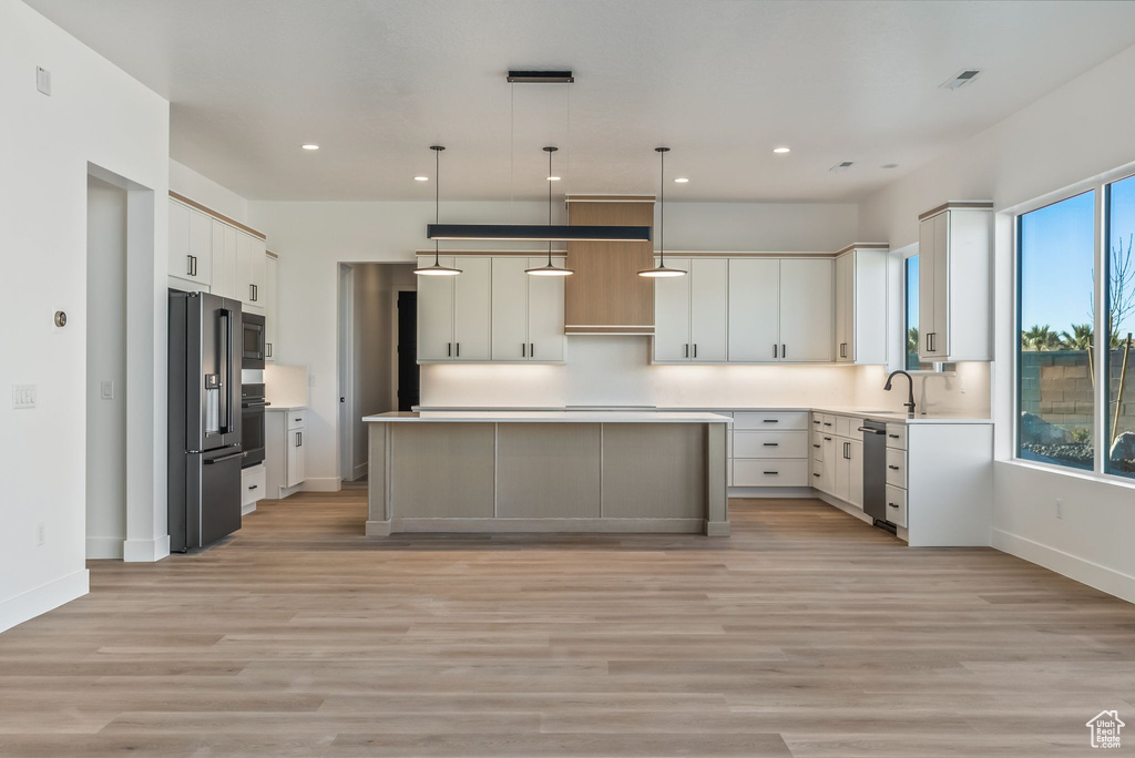 Kitchen featuring white cabinetry, light hardwood / wood-style flooring, a kitchen island, pendant lighting, and stainless steel appliances