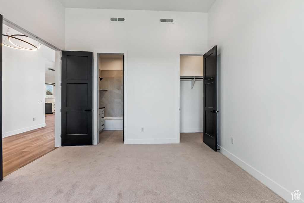 Unfurnished bedroom featuring a walk in closet, ensuite bath, a closet, and carpet