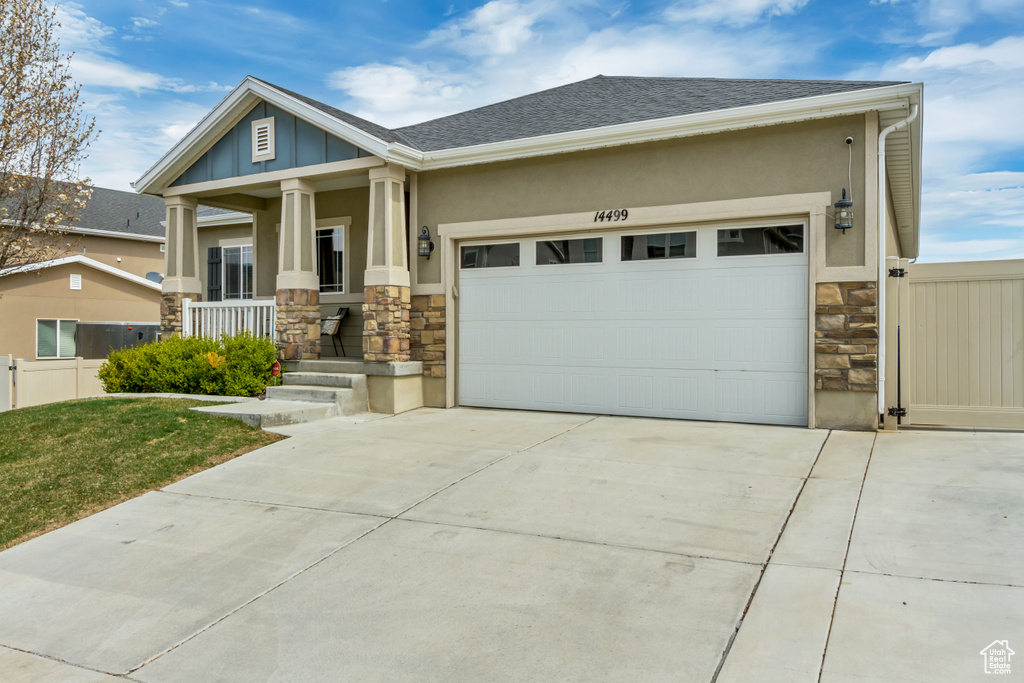 Craftsman-style house with covered porch, stucco siding, concrete driveway, and stone siding