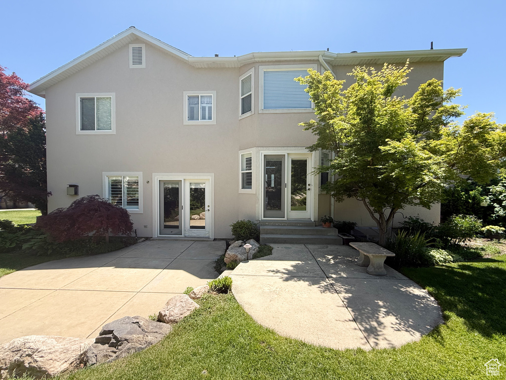 Rear view of house featuring stucco siding, a patio, a yard, and entry steps