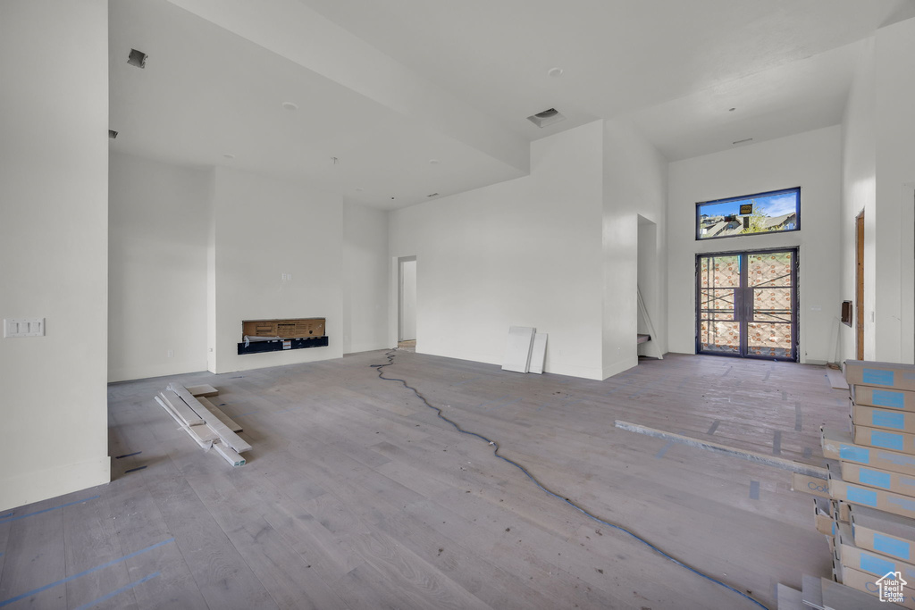 Unfurnished living room featuring a towering ceiling, wood finished floors, and baseboards