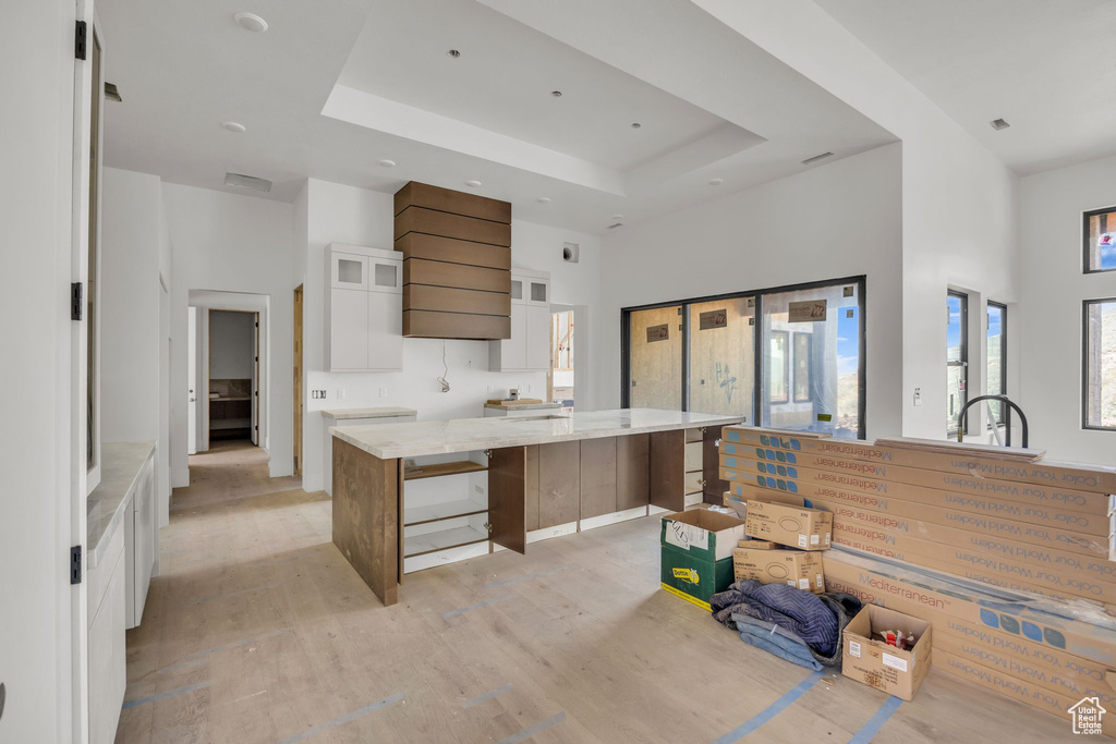 Kitchen with light wood-style floors, white cabinetry, a high ceiling, a tray ceiling, and glass insert cabinets