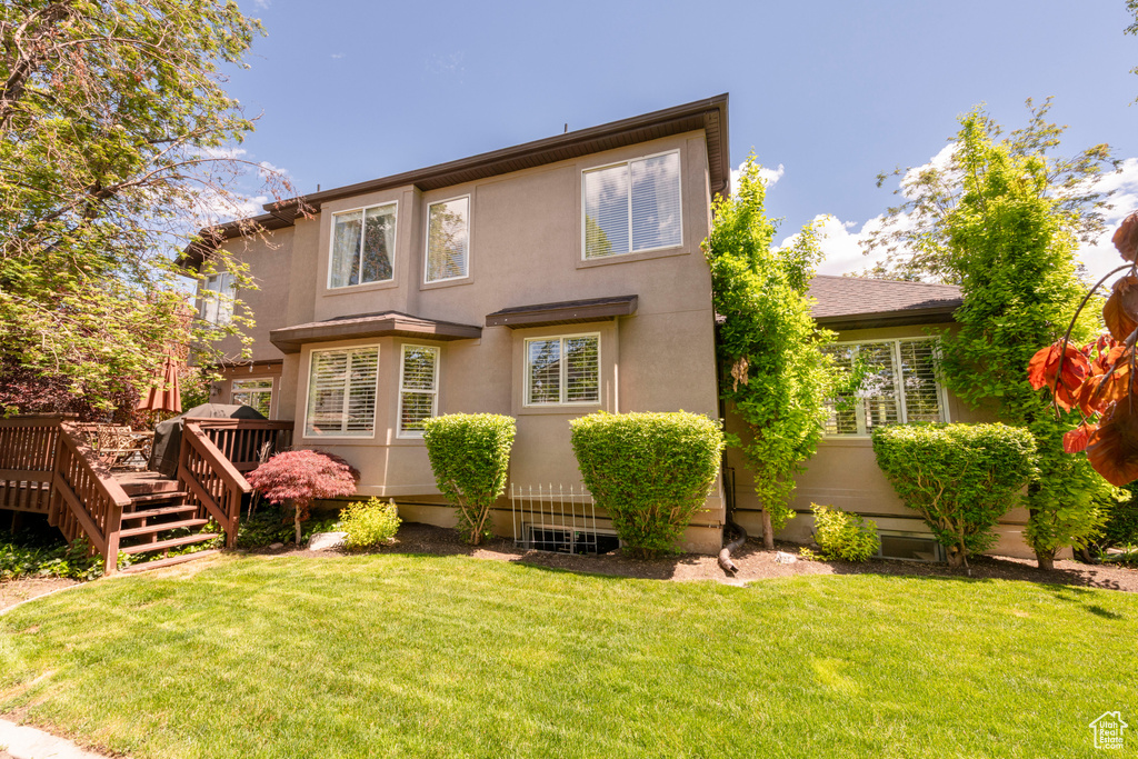Rear view of house featuring a deck, stucco siding, and a yard