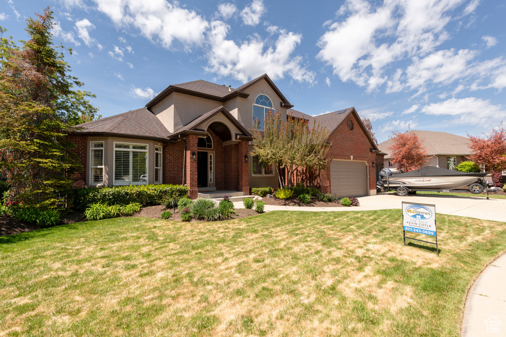 Traditional home featuring brick siding, driveway, an attached garage, and a front yard