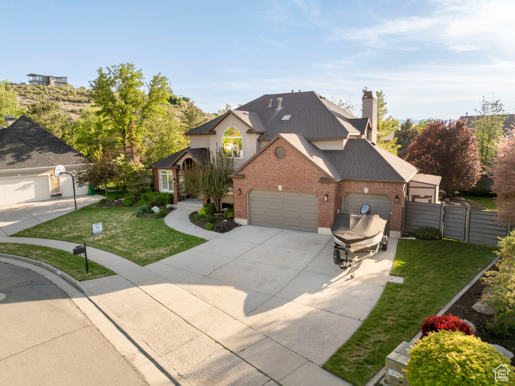 Traditional-style house featuring brick siding, driveway, an attached garage, a gate, and roof with shingles