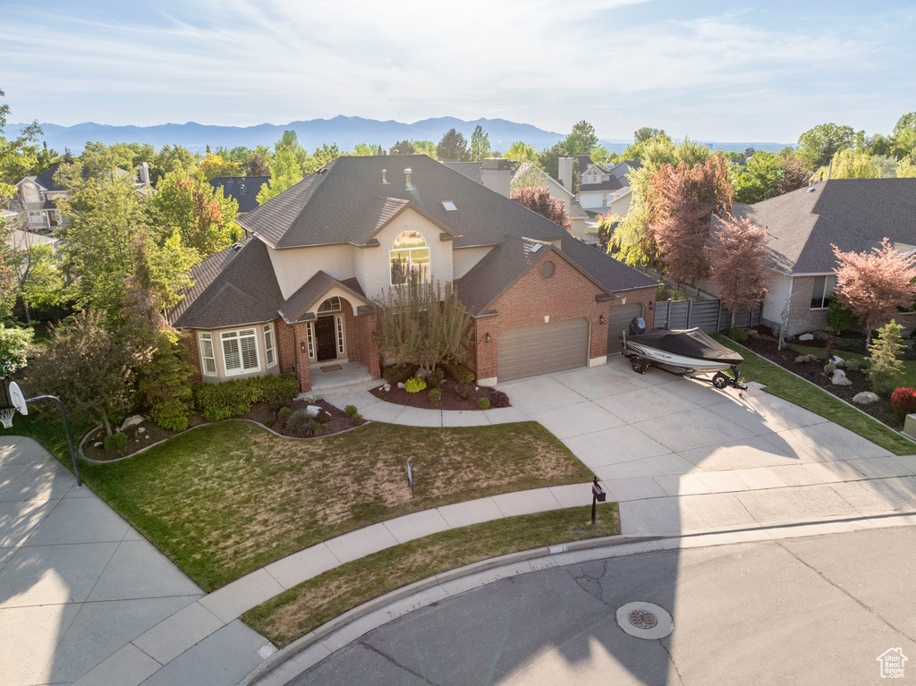 View of front of property featuring concrete driveway, brick siding, an attached garage, a front yard, and a mountain view