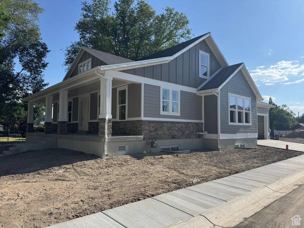 View of front of house featuring board and batten siding, covered porch, stone siding, and driveway