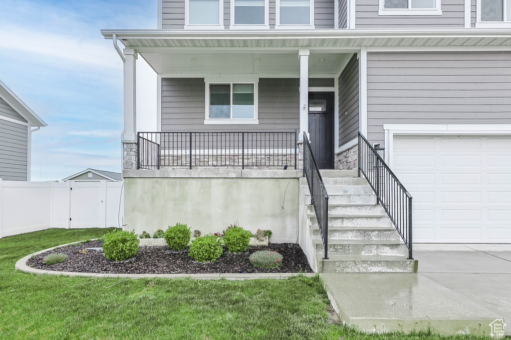 Entrance to property featuring an attached garage, covered porch, concrete driveway, and stone siding