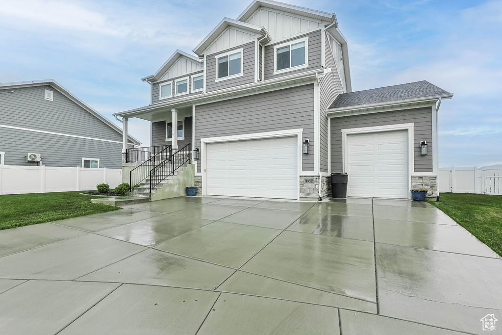 View of front facade with board and batten siding, driveway, stone siding, an attached garage, and a porch