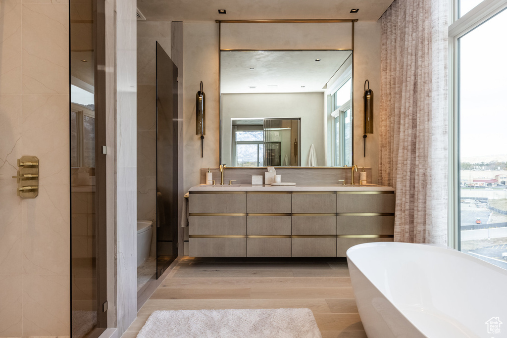 Bathroom featuring wood finished floors, a freestanding bath, double vanity, and toilet