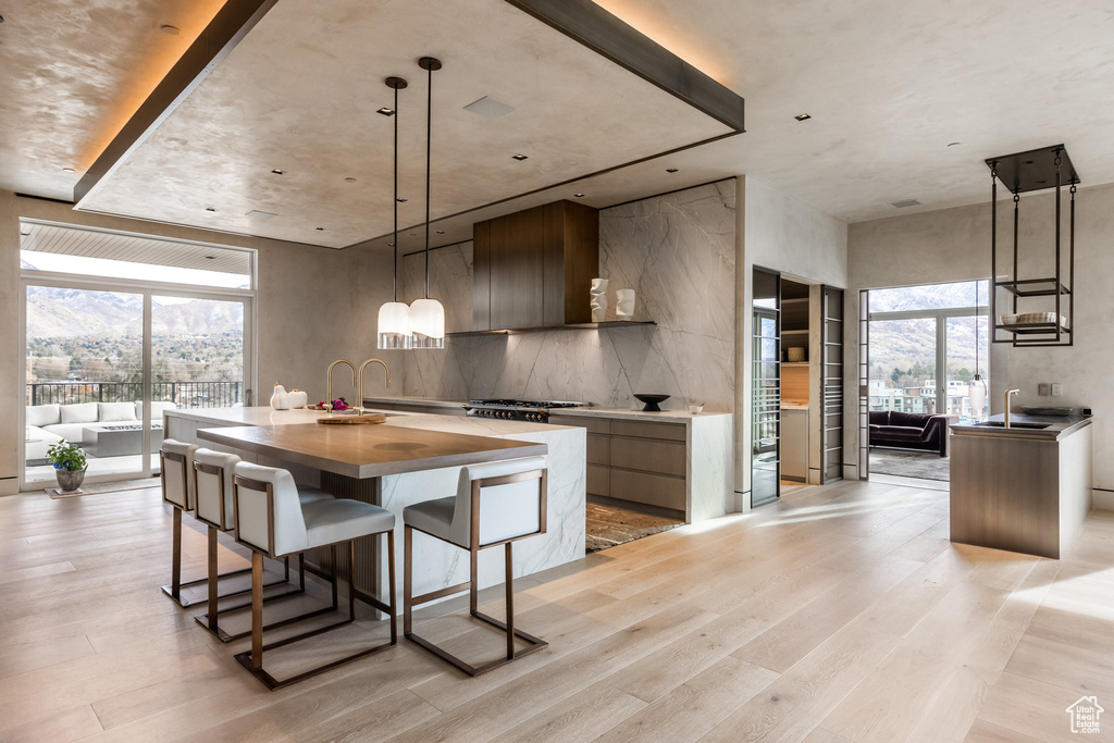 Kitchen featuring modern cabinets, an island with sink, light wood-type flooring, a sink, and a breakfast bar area