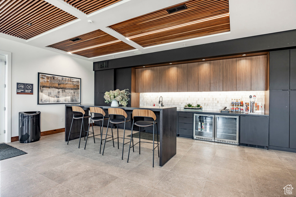 Indoor bar with wine cooler, tasteful backsplash, light tile patterned floors, and baseboards