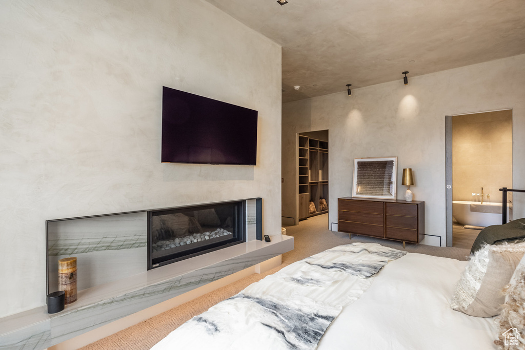Carpeted bedroom featuring a glass covered fireplace, a spacious closet, and ensuite bath