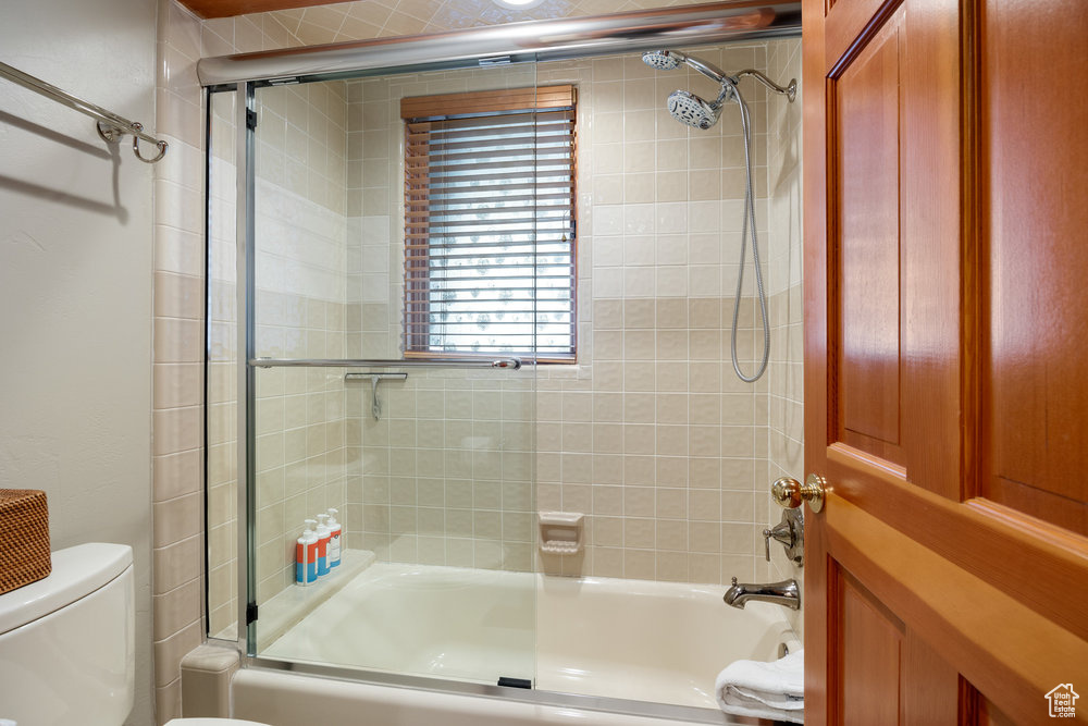 Bathroom with shower / bath combination with glass door and toilet