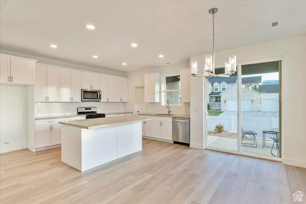 Kitchen with decorative light fixtures, white cabinets, a center island, stainless steel appliances, and a healthy amount of sunlight