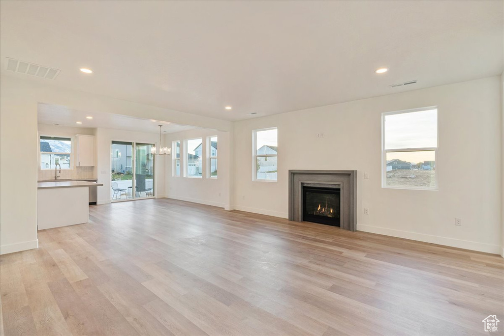 Unfurnished living room featuring sink, a notable chandelier, and light wood-type flooring