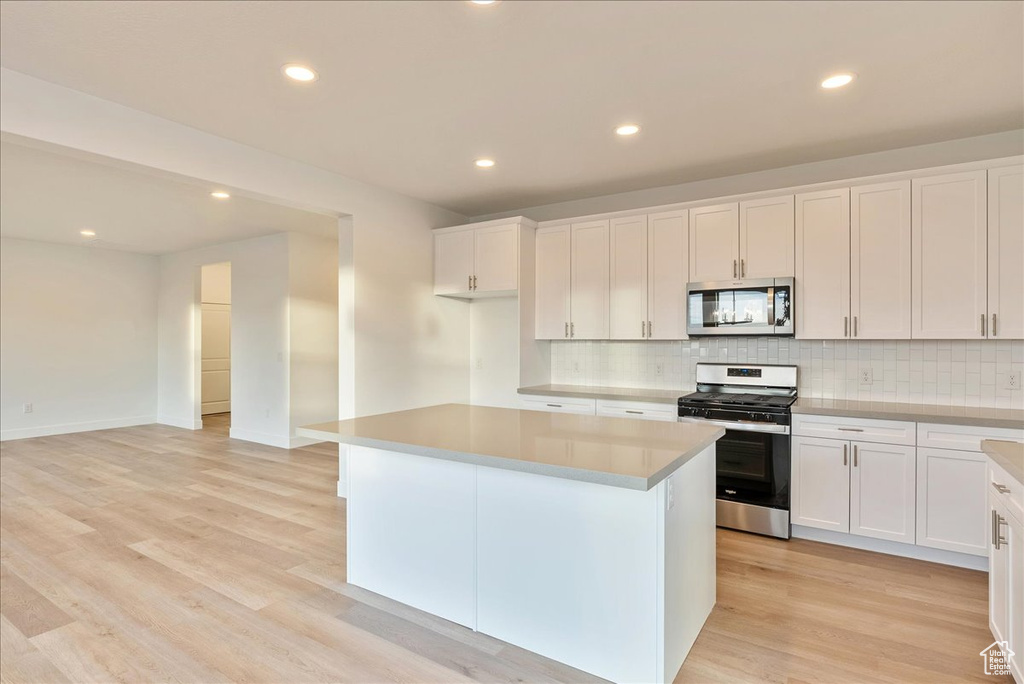 Kitchen with light hardwood / wood-style flooring, a kitchen island, white cabinets, and appliances with stainless steel finishes