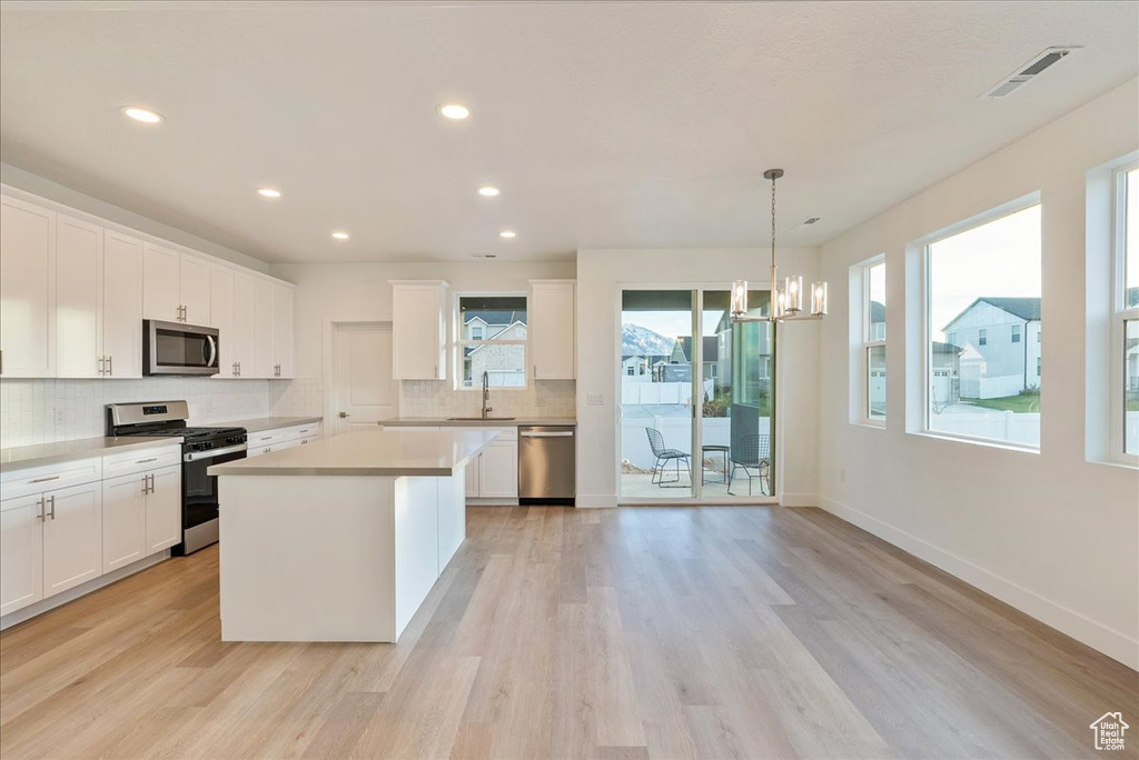 Kitchen with white cabinetry, a center island, hanging light fixtures, appliances with stainless steel finishes, and light hardwood / wood-style floors