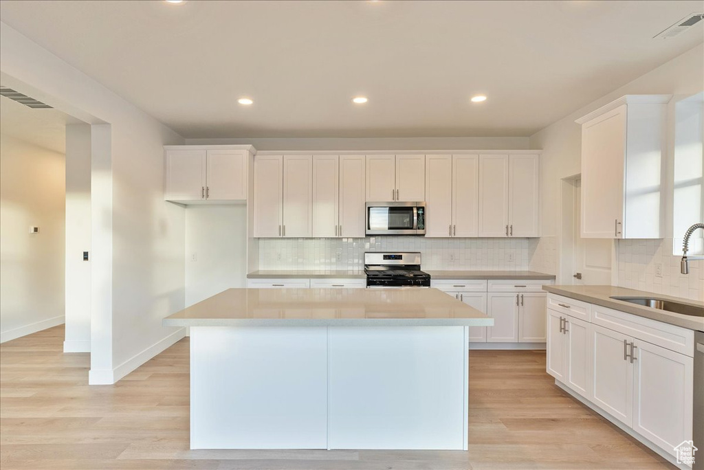 Kitchen with sink, a center island, appliances with stainless steel finishes, light hardwood / wood-style floors, and white cabinets