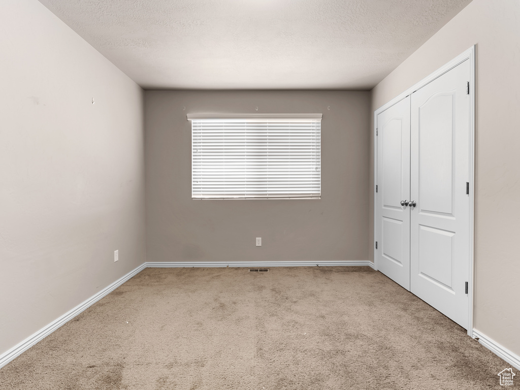 Unfurnished bedroom featuring light colored carpet, a closet, and a textured ceiling