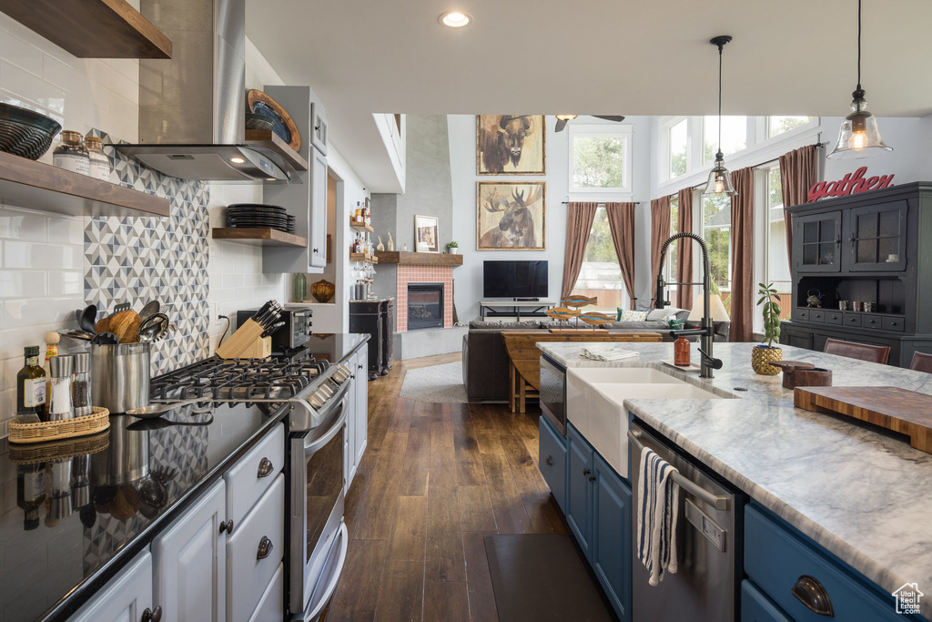 Kitchen with open shelves, a sink, wall chimney exhaust hood, stainless steel appliances, and blue cabinets