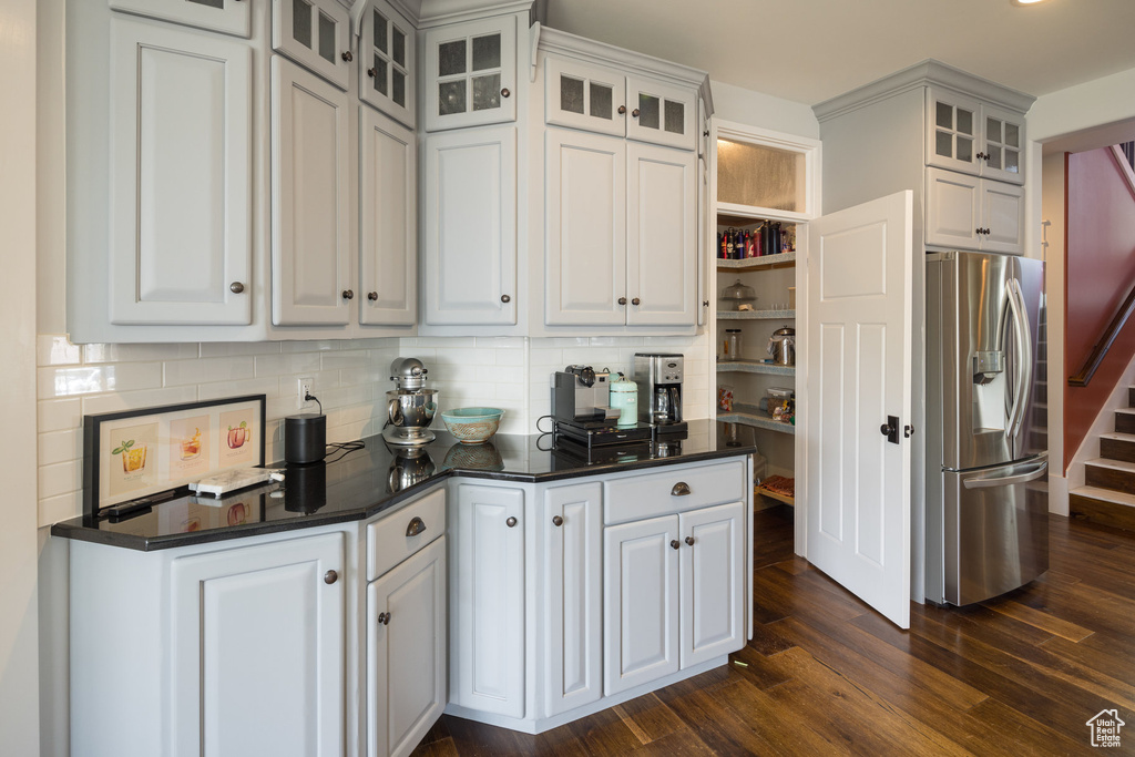 Kitchen featuring stainless steel fridge, decorative backsplash, dark wood-type flooring, and dark countertops