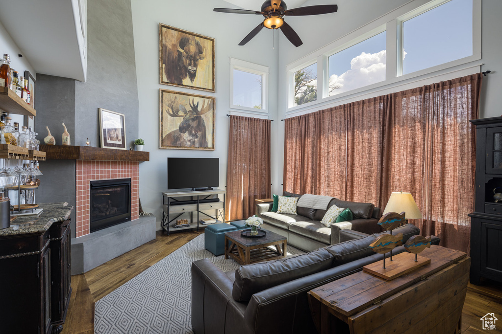 Living room with a tiled fireplace, ceiling fan, wood finished floors, and a high ceiling