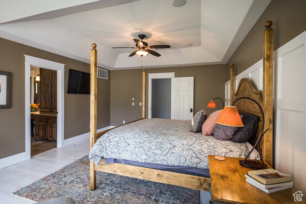 Bedroom with baseboards, wood finished floors, ensuite bathroom, a tray ceiling, and visible vents