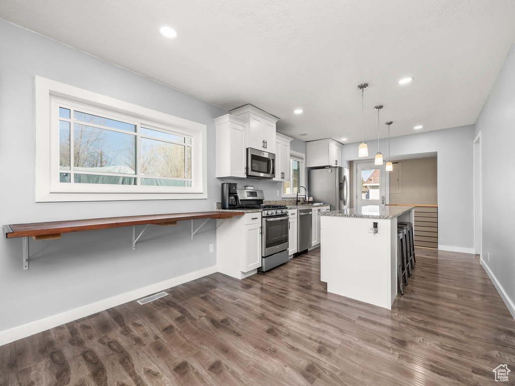 Kitchen with white cabinetry, hanging light fixtures, a breakfast bar, and appliances with stainless steel finishes