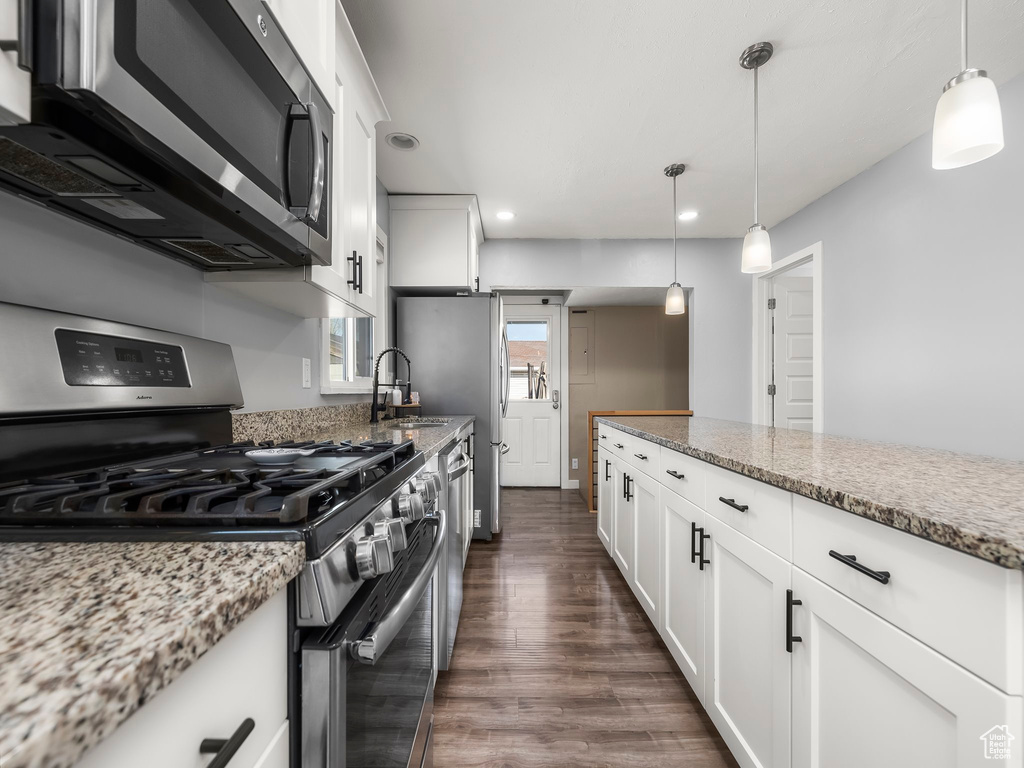 Kitchen with dark wood-type flooring, decorative light fixtures, stainless steel appliances, light stone countertops, and white cabinets