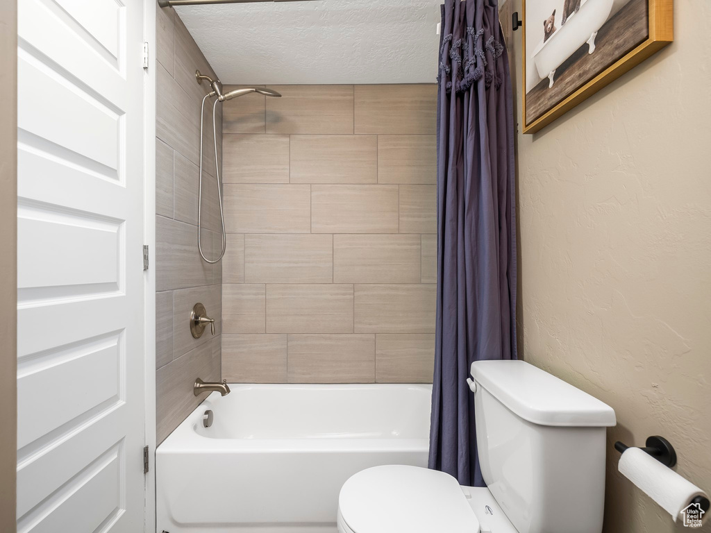 Bathroom featuring shower / tub combo with curtain, toilet, and a textured ceiling