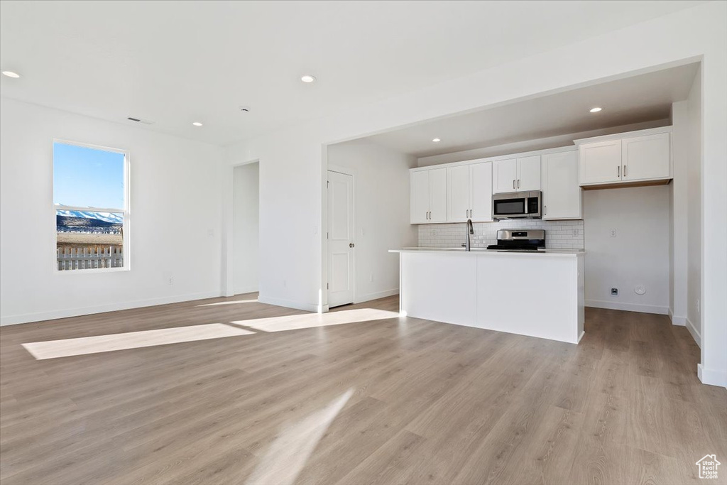 Kitchen featuring a center island with sink, appliances with stainless steel finishes, white cabinets, light hardwood / wood-style floors, and backsplash