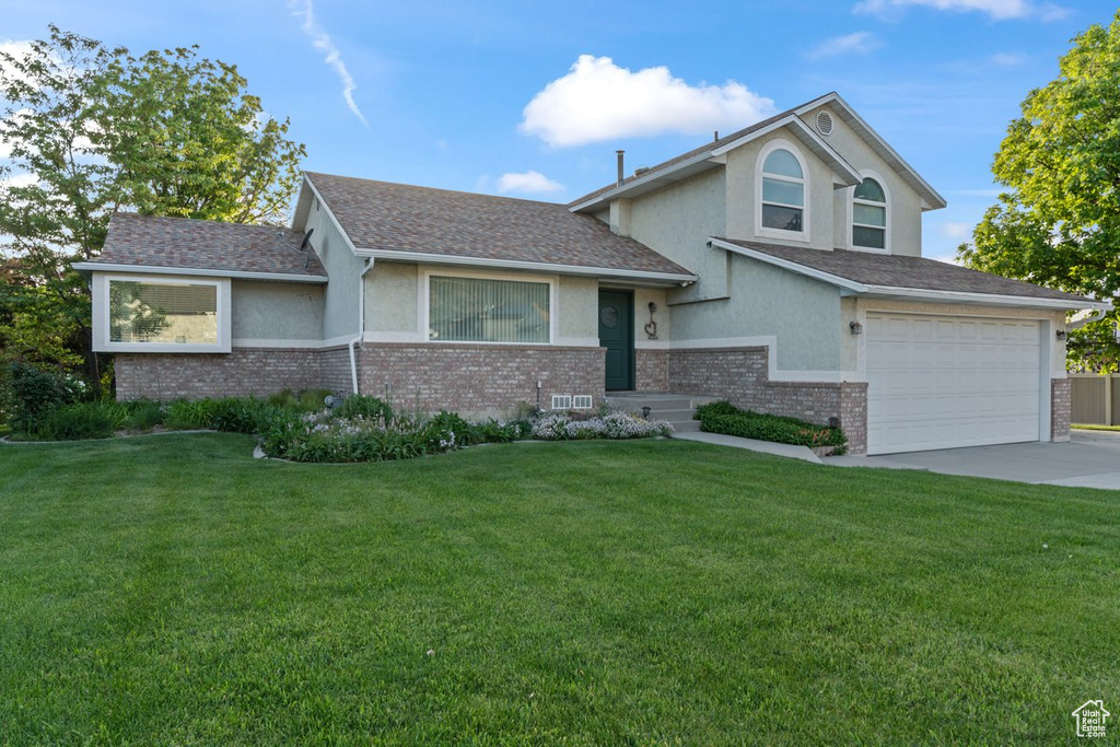 Split level home featuring stucco siding, concrete driveway, a garage, brick siding, and a front yard